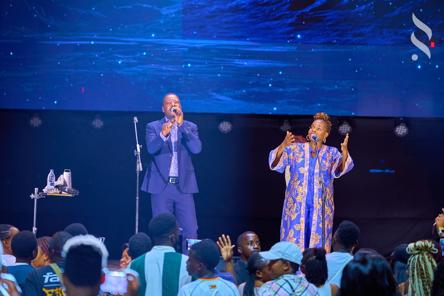 Two singers performing on a blue-lit stage to a crowd, shot by Simply Art Creative